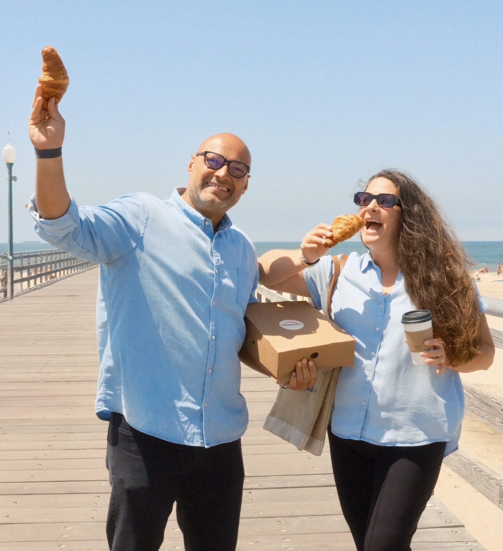 Partners eating croissant on pier by ocean